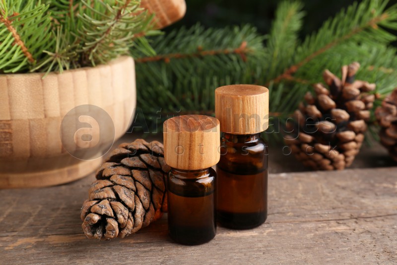 Photo of Bottles of pine essential oil, conifer tree branches and cones on wooden table