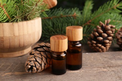 Bottles of pine essential oil, conifer tree branches and cones on wooden table