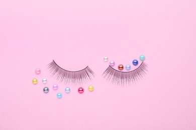 Photo of False eyelashes and colorful beads on pink background, flat lay