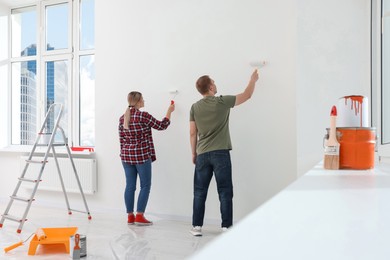 Couple painting wall in apartment during repair, back view