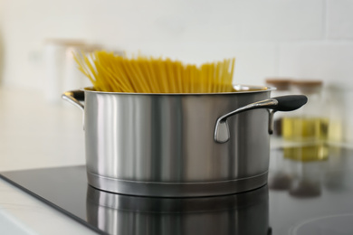 Saucepan with uncooked pasta on stove in kitchen, closeup
