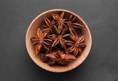 Aromatic anise stars in wooden bowl on grey background, top view