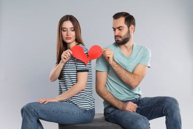 Couple tearing paper heart on light grey background. Relationship problems