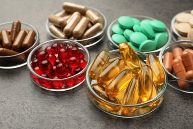 Photo of Different dietary supplements in glass bowls on grey table