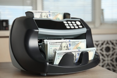 Modern electronic bill counter with money on table indoors, closeup