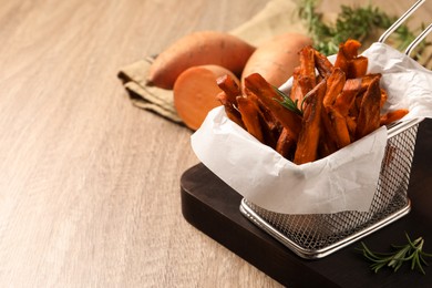 Frying basket with sweet potato fries on wooden table, closeup. Space for text