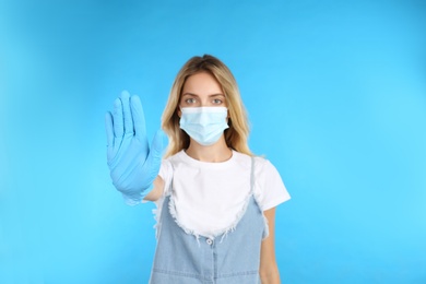 Woman in protective mask showing stop gesture on light blue background. Prevent spreading of COVID‑19
