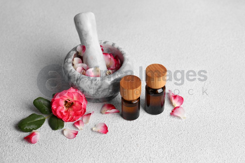 Glass bottles of aromatic essential oil, mortar with roses on white table
