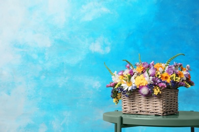 Photo of Wicker basket with beautiful wild flowers on table against color background