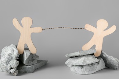 Competition concept. Wooden human figures on stones tugging rope against grey background