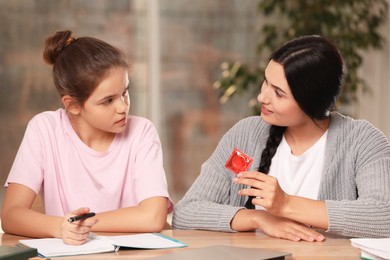Photo of Mother talking with her teenage daughter about contraception while she doing homework at home. Sex education concept