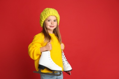 Cute little girl in yellow knitted sweater with skates on red background, space for text