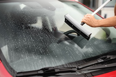 Man cleaning windshield with glass wiper, closeup. Car wash service