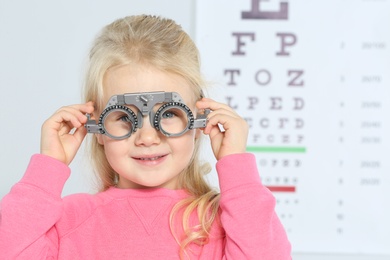 Little girl with trial frame near eye chart in hospital, space for text. Visiting children's doctor