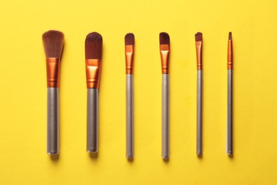 Different makeup brushes on yellow background, flat lay
