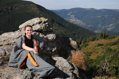 Happy tourist in sleeping bag on mountain peak