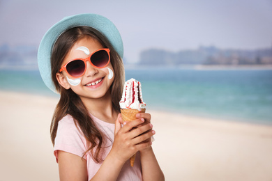 Image of Adorable little girl with sun protection cream on face at sandy beach, space for text 