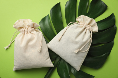 Cotton eco bags and monstera leaf on green background, flat lay