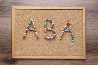 Applied behavior analysis concept. Corkboard with abbreviation ABA made of colorful pins on wooden table, top view