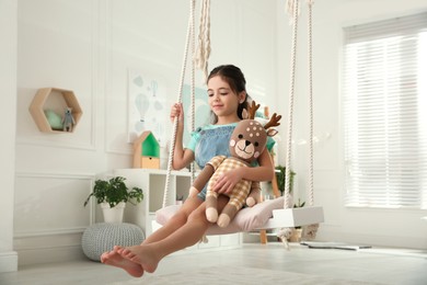 Cute little girl playing with toy deer on swing at home