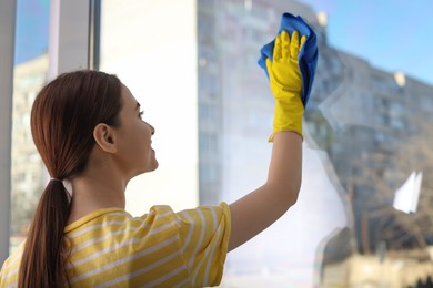 Young woman cleaning window glass with rag at home