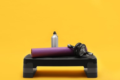 Step platform, mat, bottle of water and abdominal wheel on yellow background. Sports equipment