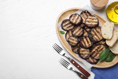 Delicious grilled eggplant slices served on white wooden table, flat lay. Space for text