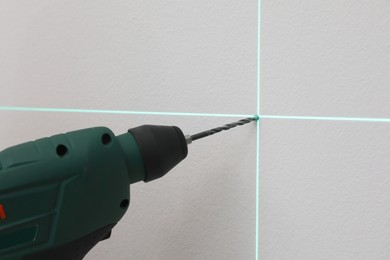 Using cross line laser level for accurate measurement and drilling hole in grey wall, closeup