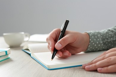 Woman writing in notebook at wooden table in office, closeup