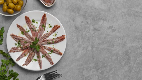 Photo of Delicious anchovy fillets, served with olives and parsley on grey table, flat lay. Space for text