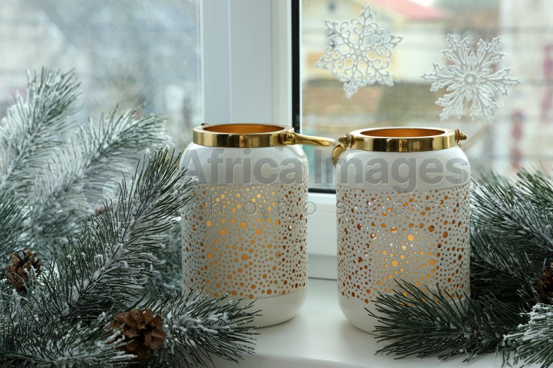 Photo of Beautiful lanterns with burning candles and fir tree branches on window sill. Christmas decor