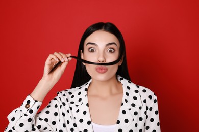 Photo of Funny woman making fake mustache with her hair on red background