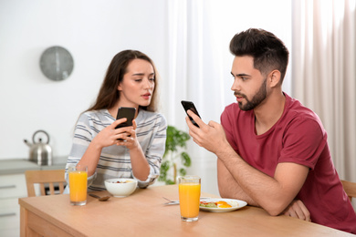 Distrustful young woman peering into boyfriend's smartphone at home