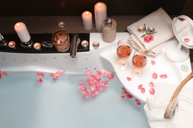 Bathtub with glasses of wine and candles indoors, above view. Romantic atmosphere
