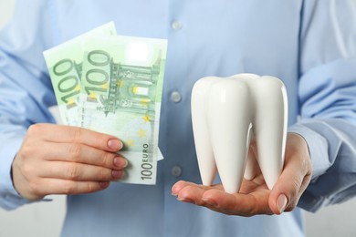 Woman holding ceramic model of tooth and euro banknotes on light background, closeup. Expensive treatment