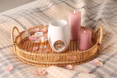 Wicker tray with aroma lamp, bottle of oil and burning candles on bed