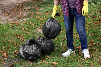 Man holding plastic bags with garbage in park, closeup.