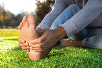 Man sitting barefoot on fresh green grass outdoors, closeup