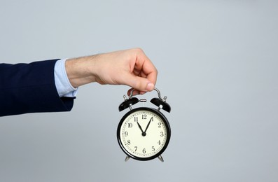 Closeup view of businessman holding alarm clock on grey background, space for text. Time management