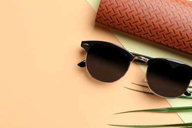 Stylish sunglasses and brown leather case with pattern on beige background, top view. Space for text