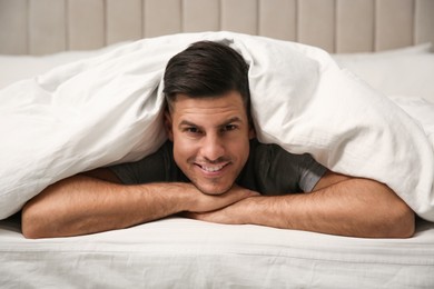 Handsome man relaxing under soft blanket in bed at home