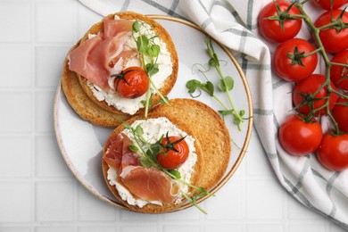 Tasty rusks with prosciutto, cream cheese and tomatoes on white table, flat lay