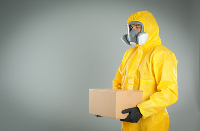 Man wearing chemical protective suit with cardboard box on light grey background, space for text. Prevention of virus spread
