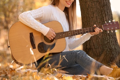 Teen girl playing guitar in autumn park, closeup