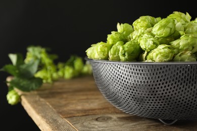 Photo of Fresh green hops on wooden table against black background, closeup. Space for text