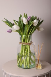 Photo of Beautiful bouquet of colorful tulips in glass vase and reed freshener on table against pink background