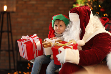 Santa Claus and little boy with Christmas gifts indoors