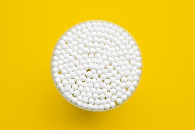 Many cotton buds in container on yellow background, top view