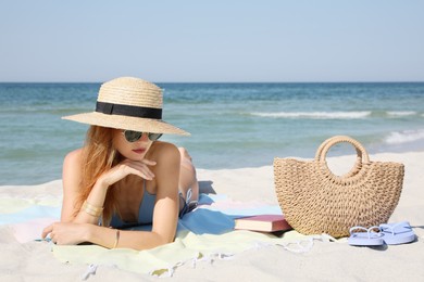 Beautiful woman with bag and other beach stuff on sand near sea