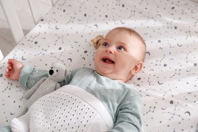 Adorable happy baby with toy lying in crib